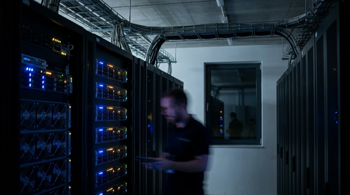 A dimly lit server room with rows of blinking hardware racks casting blue and amber light across the floor.